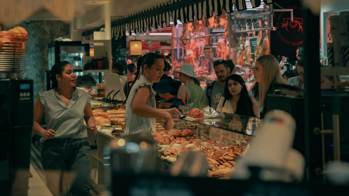 Mostrador de una panadería en una plaza de mercado con los productos ordenados y clientes esperando