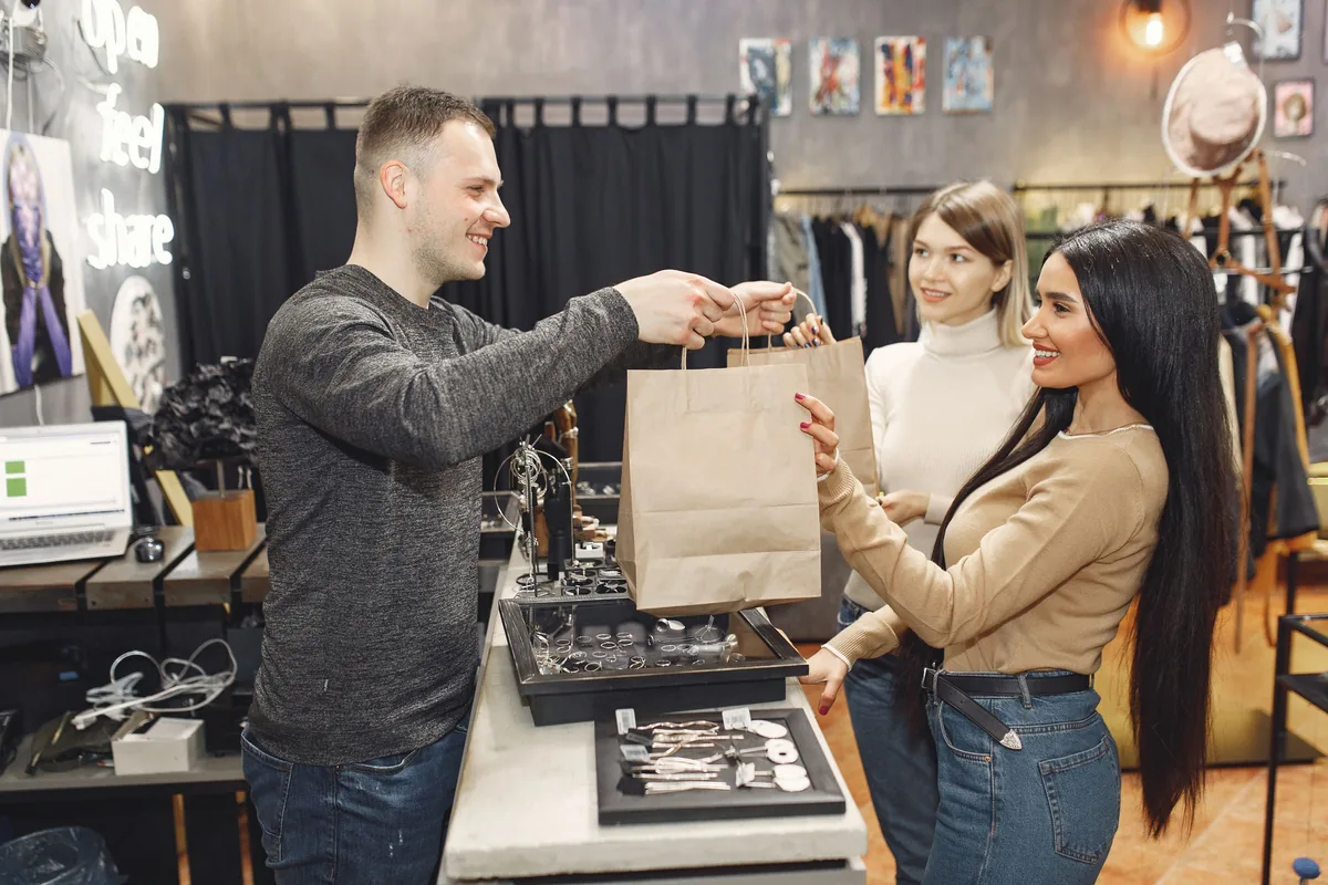 Vendedor entregando una bolsa con productos a dos clientas en su puesto
